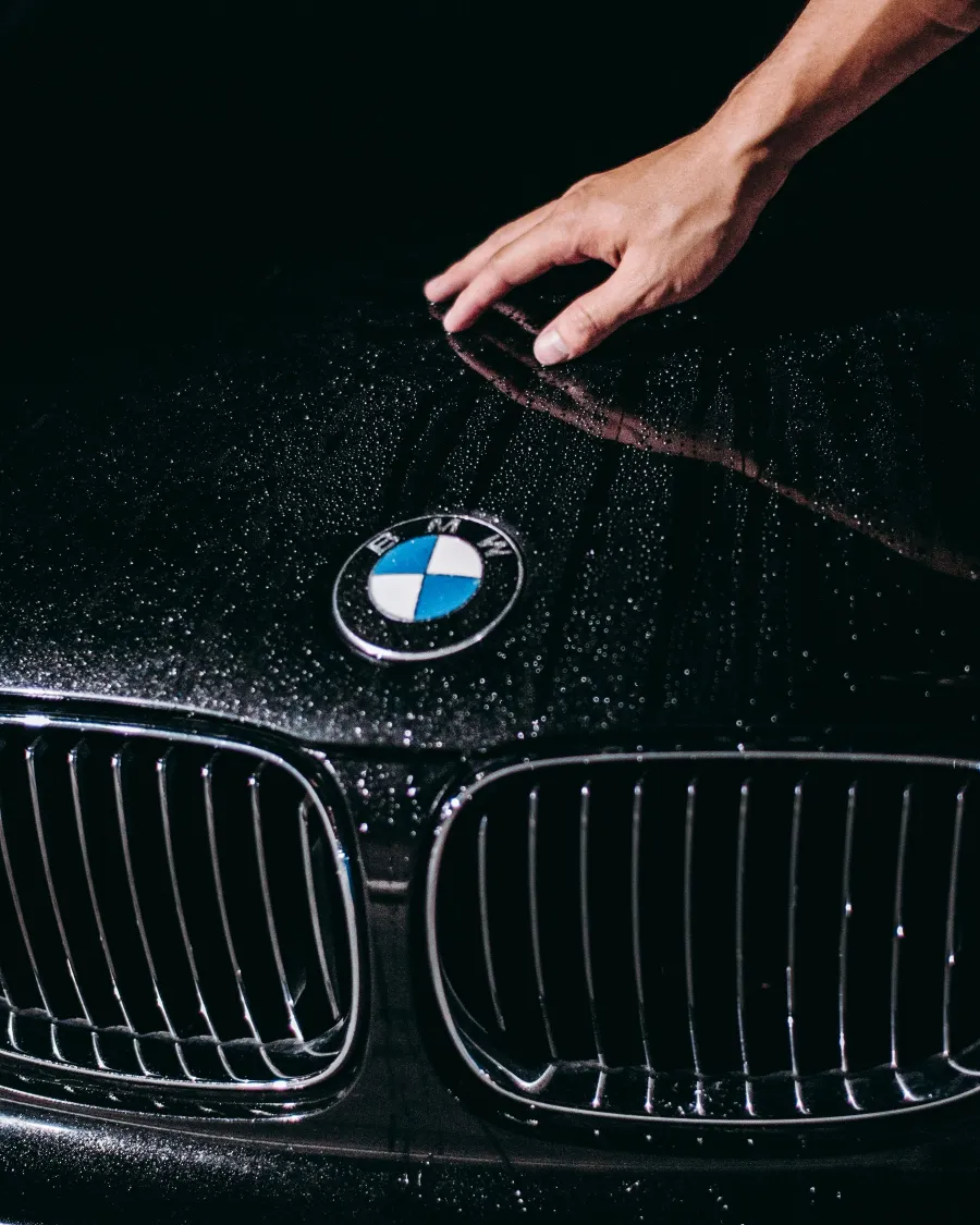 Detailer's hand on the wet hood of a black BMW